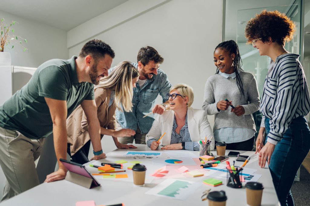 Six personnes discutant d'un projet autour d'un bureau de travail, séance de brainstorm.